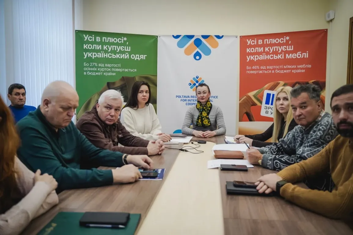 У конференц-залі за столом сидять десятеро учасників зустрічі — по п’ять з кожного боку. На задньому плані — три банери. Лівий зелений закликає купувати український одяг, адже 27% його вартості повертається в бюджет. Центральний — з логотипом Полтавського регіонального офісу міжнародного співробітництва. Правий червоний — про українські меблі, з акцентом на 46% повернення до бюджету. Атмосфера — ділова, спрямована на підтримку місцевого виробництва.