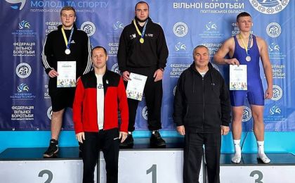 Троє борців стоять на п'єдесталі після завершення чемпіонату Полтавської області з вільної боротьби. Переможець — у центрі на найвищій сходинці з медаллю та грамотою. Спортсмени, які посіли друге і третє місця, стоять ліворуч і праворуч відповідно, також з нагородами. Перед п'єдесталом — двоє чоловіків, ймовірно, тренери або представники організаторів. На фоні — банер із логотипами та написами українською мовою, що підтверджують офіційний статус змагань.