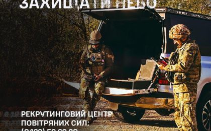 Двоє військовослужбовців у камуфляжній формі та шоломах стоять біля відкритого багажника автомобіля, ймовірно, координуючи дії або обмінюючись інформацією. Один із них користується пристроєм — можливо, планшетом або телефоном. На тлі — дерева та ґрунтова місцевість, що вказує на польові умови. У верхній частині зображення — заклик «Приєднуйся захищати небо» та контактні дані рекрутингового центру Повітряних Сил України, зокрема командування «Схід».