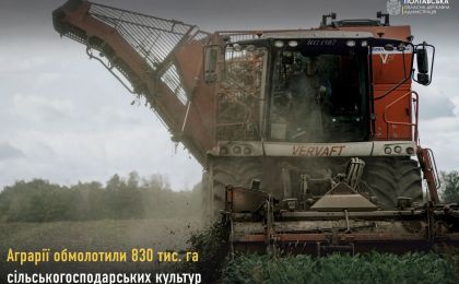 На сільськогосподарському полі працює великий червоний комбайн марки «VERVAFT», який активно збирає врожай. Видно хмару пилу та залишки рослин, що свідчить про інтенсивну роботу техніки. На задньому плані — лінія дерев і похмуре небо, що створює атмосферу осіннього дня в сільській місцевості. У верхній частині зображення — напис «Полтавська обласна державна адміністрація», а також інформація про обмолот 830 тисяч гектарів сільськогосподарських культур.